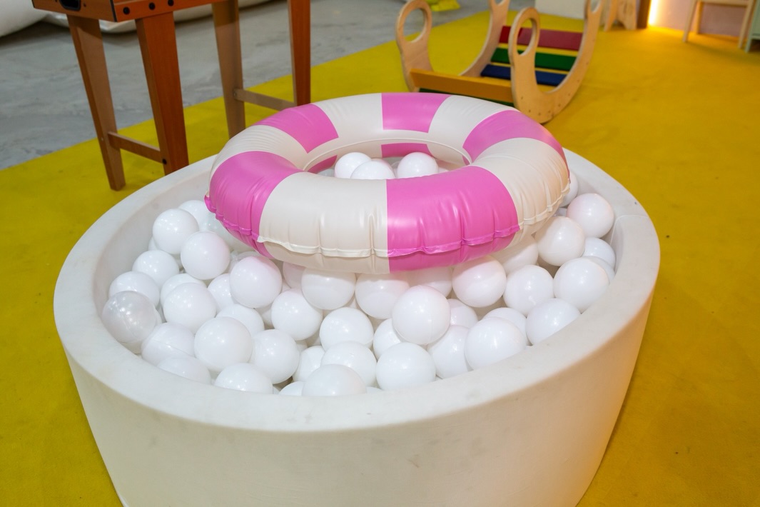Piscina de bolinhas brancas com boia rosa no piso verde