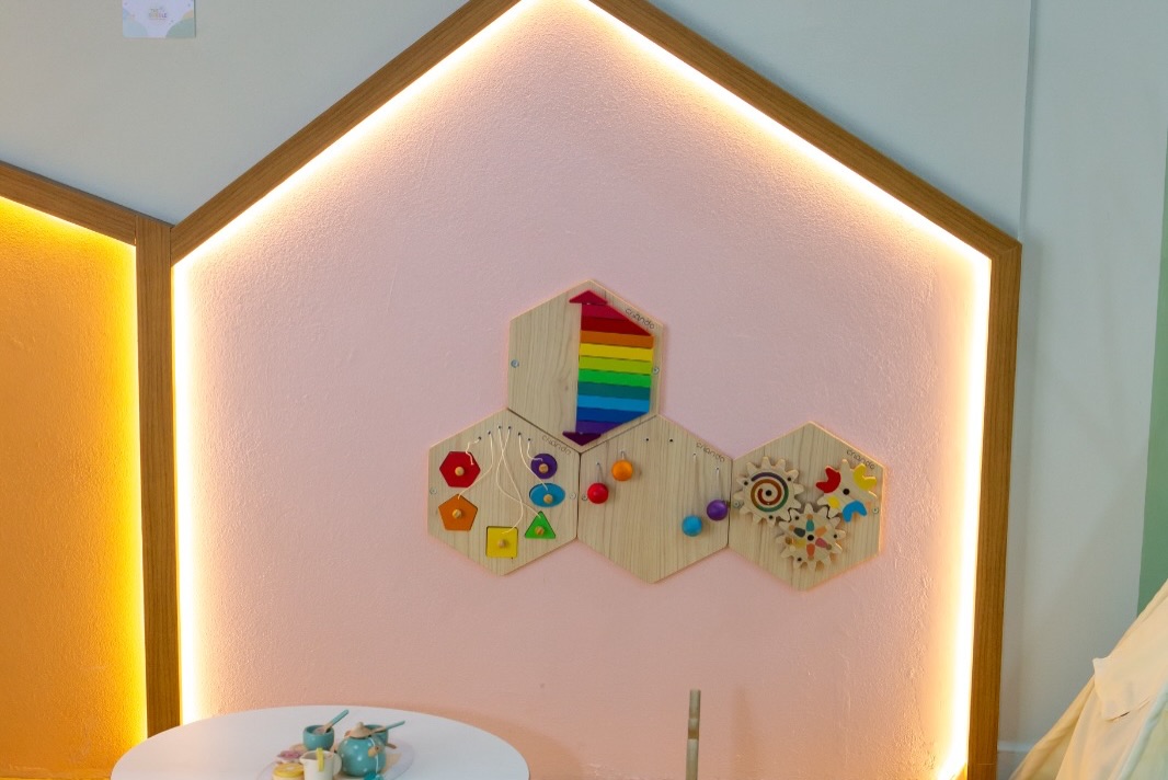 Painel de nichos hexagonais com brinquedos sensoriais e iluminação indireta